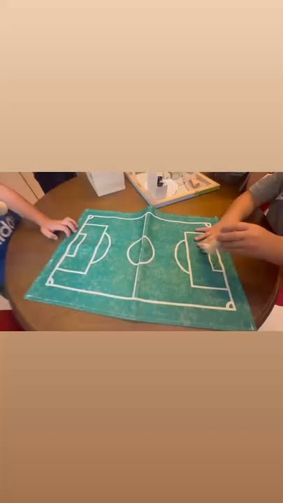 Due bambini toccano un tappeto verde con disegni di un campo da football su una tavola