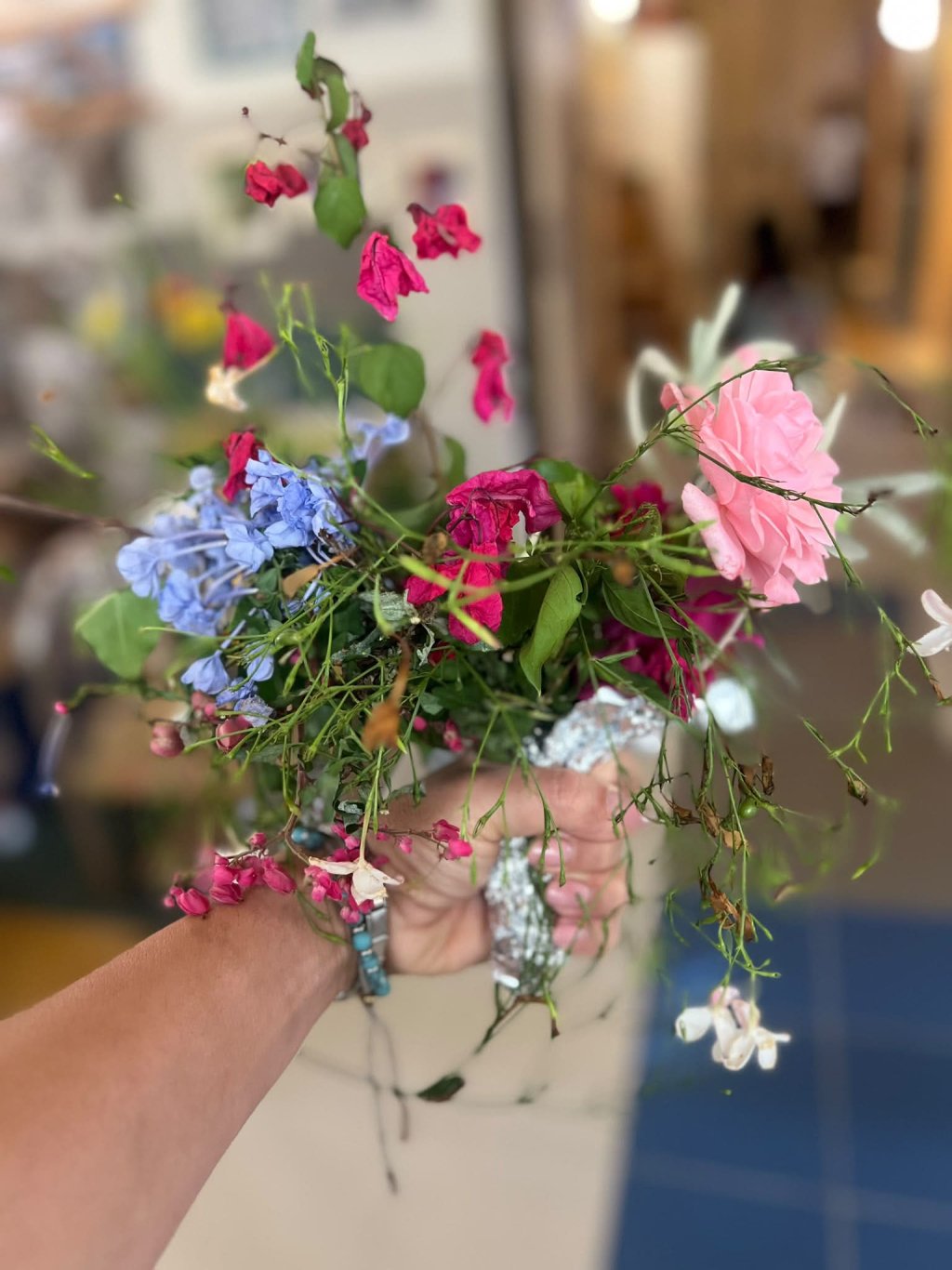 Mani tengono un bouquet di fiori colorati con rose rosa, blu e fucsia
