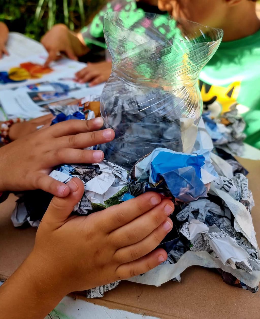 Mani di bambino che lavorano su un oggetto artigianale fatto con carta e plastica
