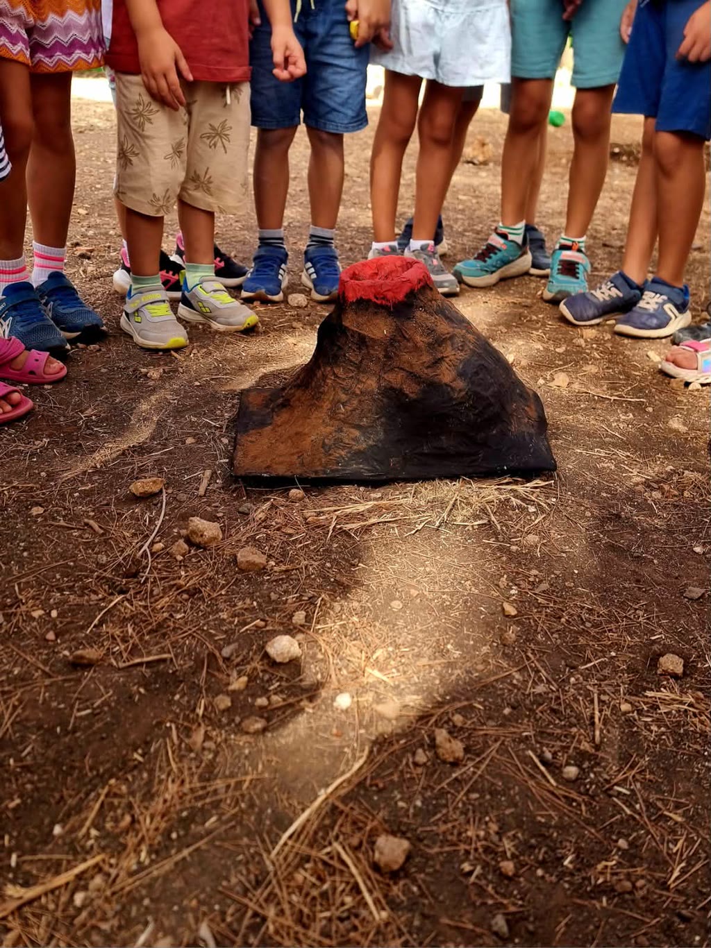 Un gruppo di bambini osserva un modello di vulcano finto con fumo rosso
