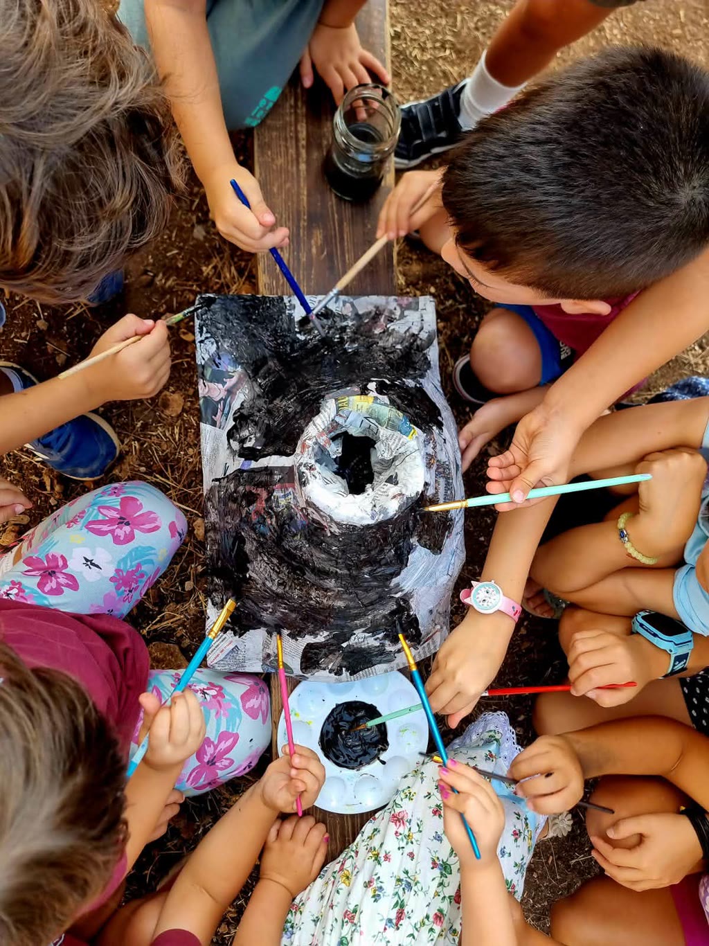 Bambini si concentrano su un dipinto con p pennelli e colori su un tavolo