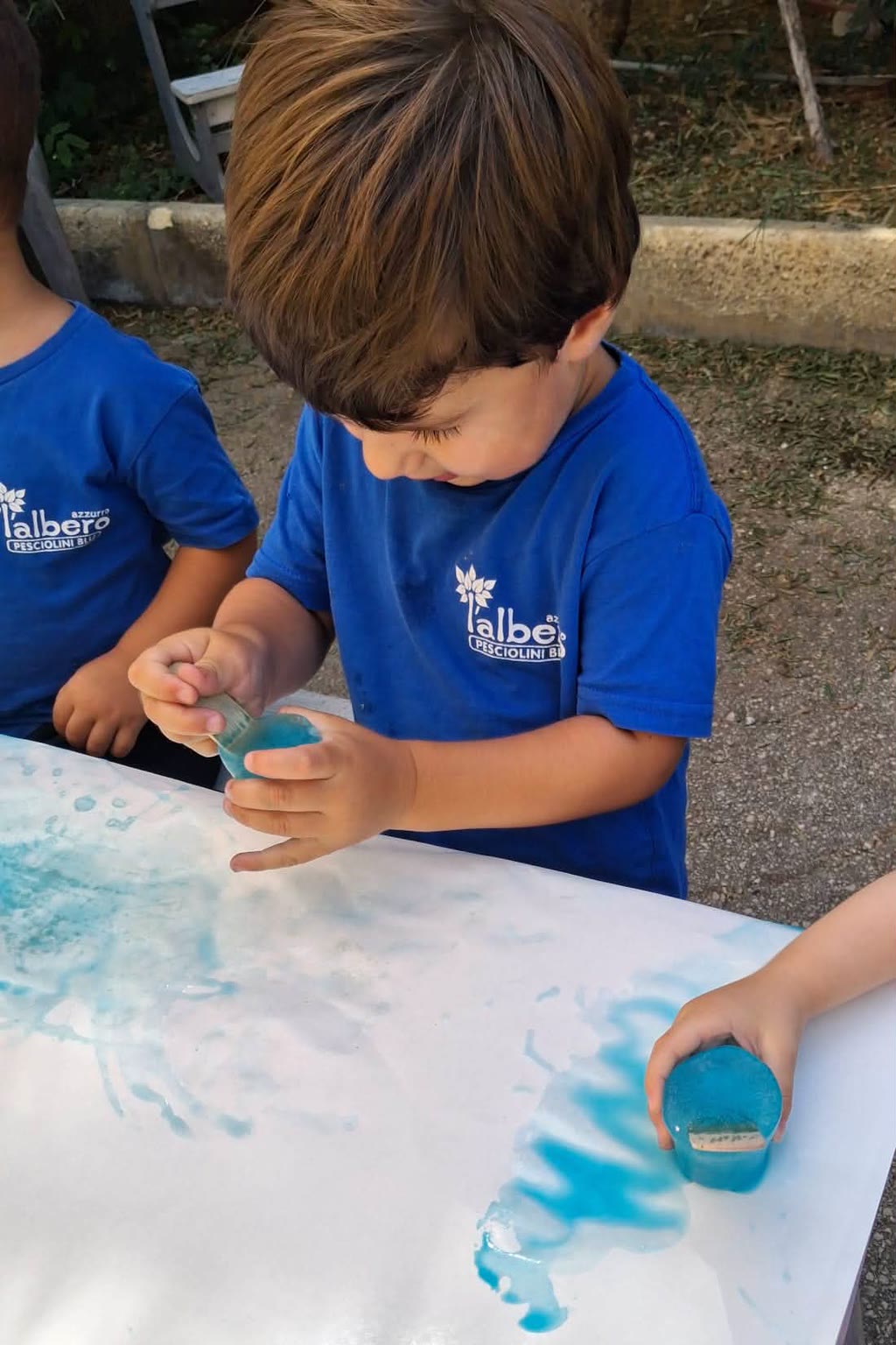 Due bambini in magliette blu stanno giocando con vernice blu su un tavolo bianco