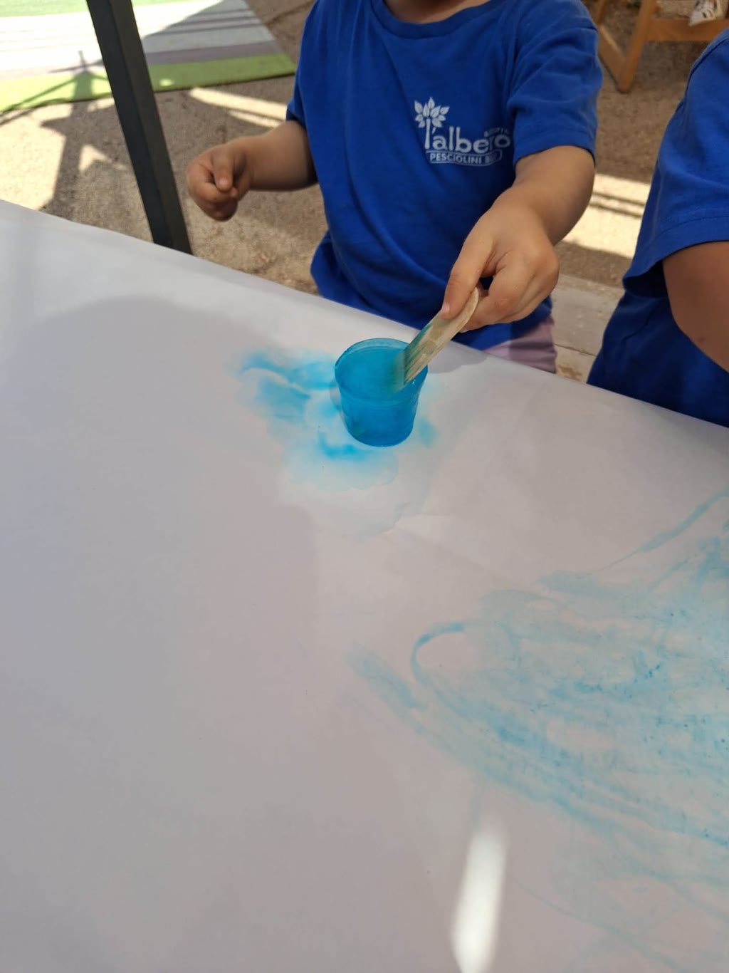 Bambino con maglietta blu dipinge su carta con pennello e colore blu