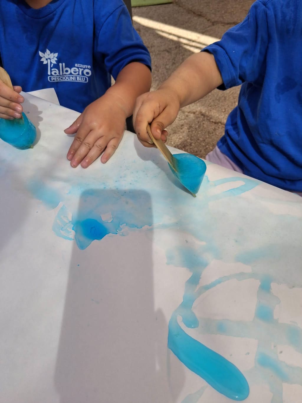 Due bambini in magliette blu stanno dipingendo con vernice blu su un grande foglio di carta