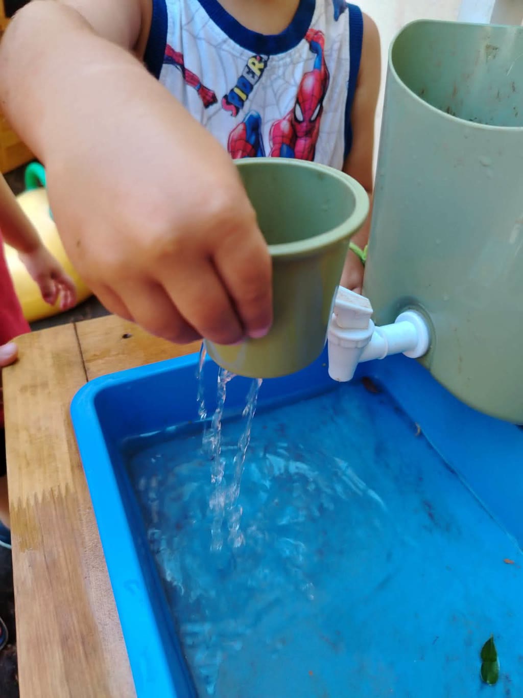 Un bambino versa acqua da un secchio in un secchio più grande