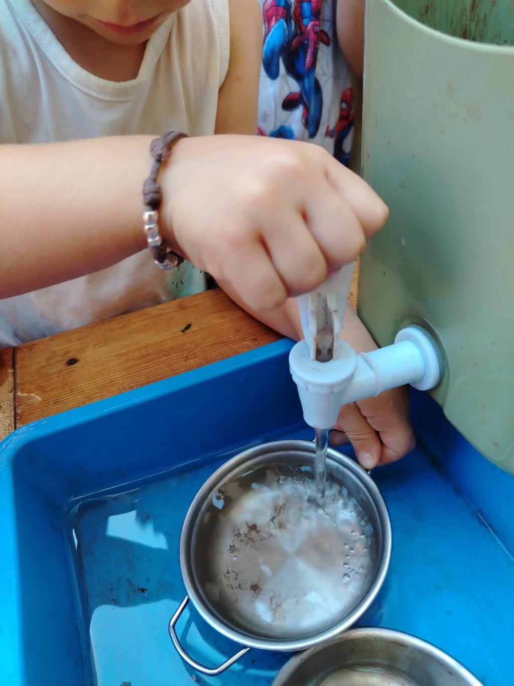 Un bambino versa acqua da un rubinetto in un pentolino