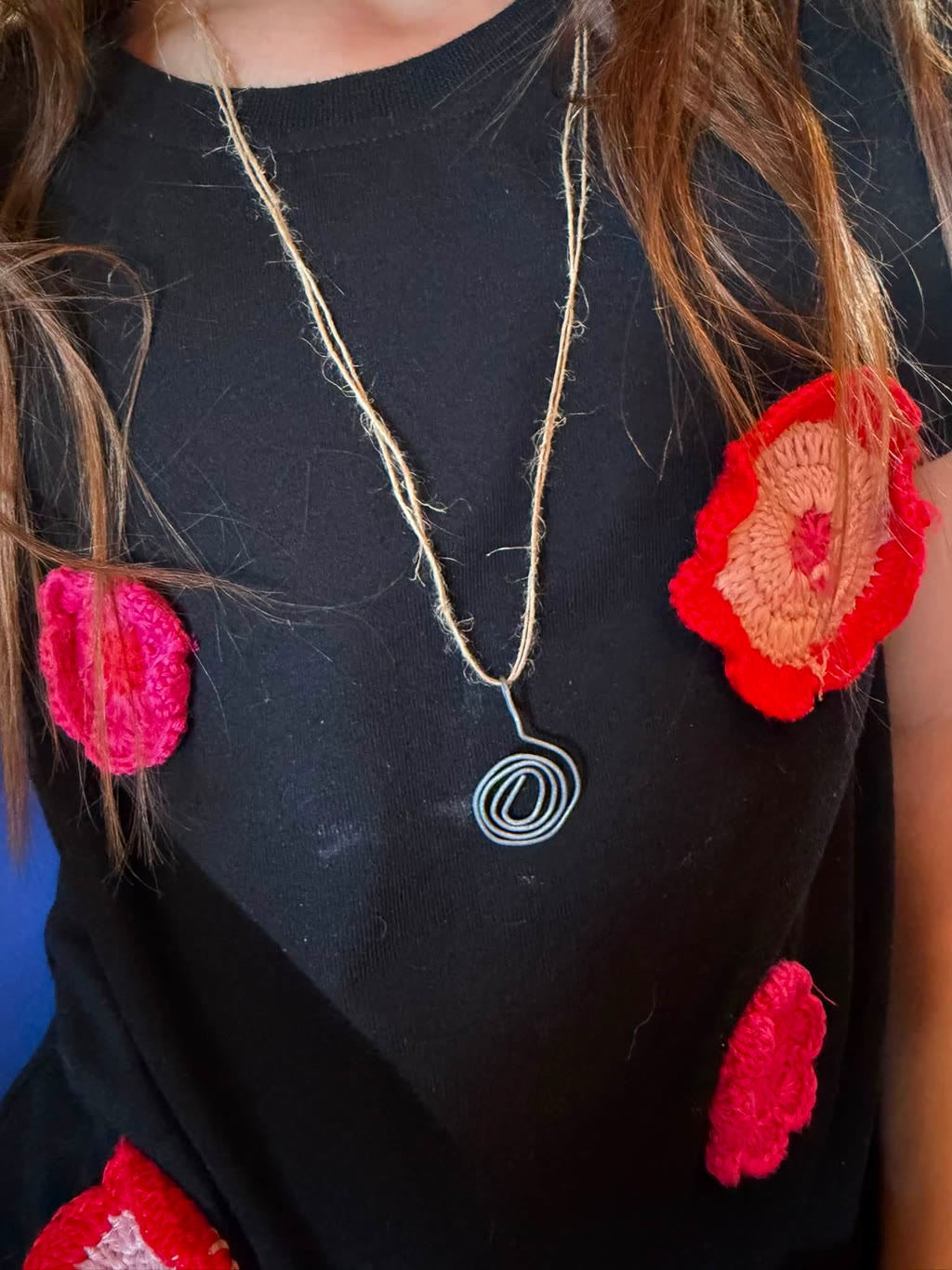Una persona indossa una maglietta nera con fiori ricamati e una collana con pendente a spirale
