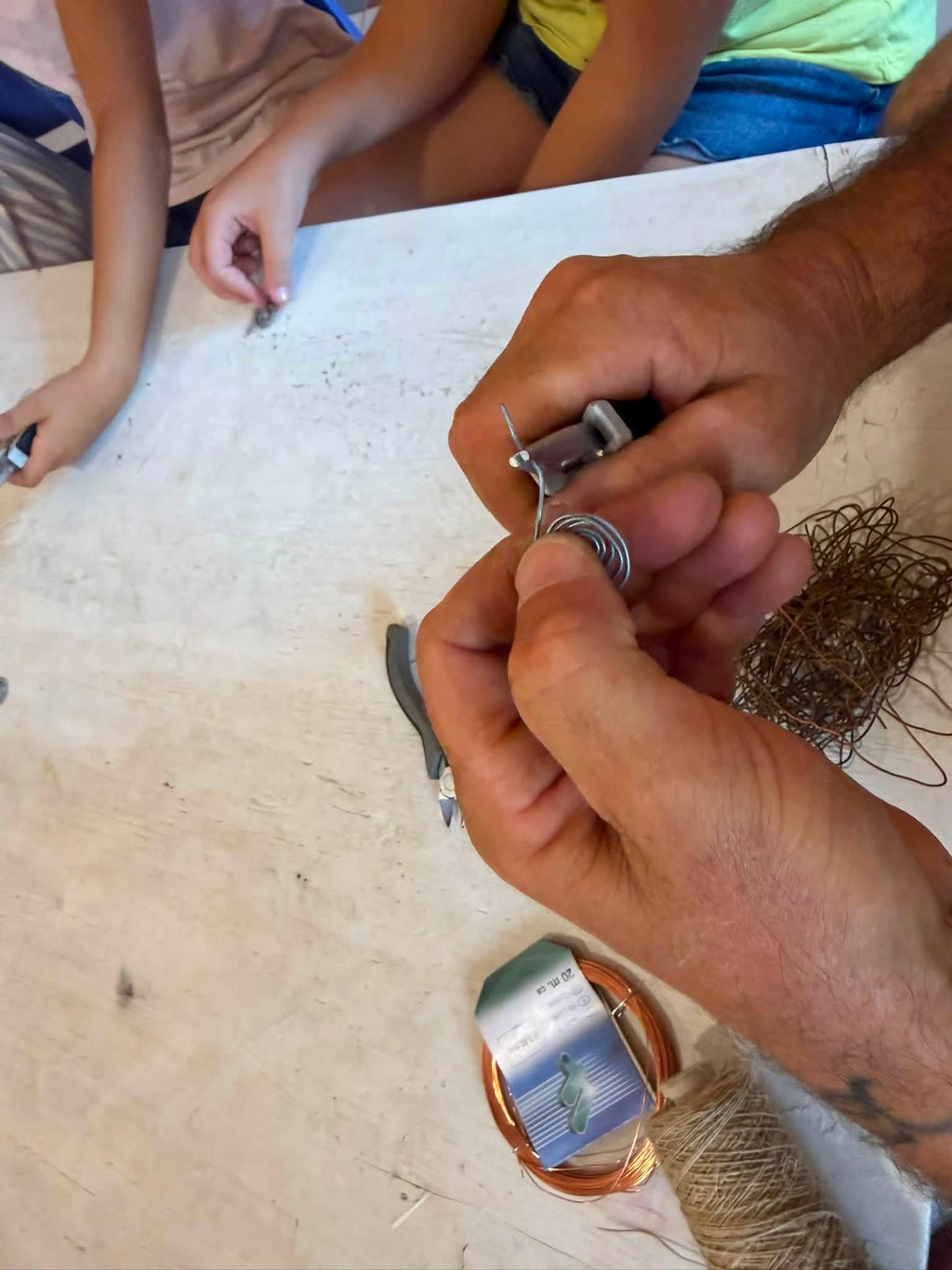 Due mani lavorano su filo avvolto su un tavolo, con un pacchetto di filo e un pacco di capelli