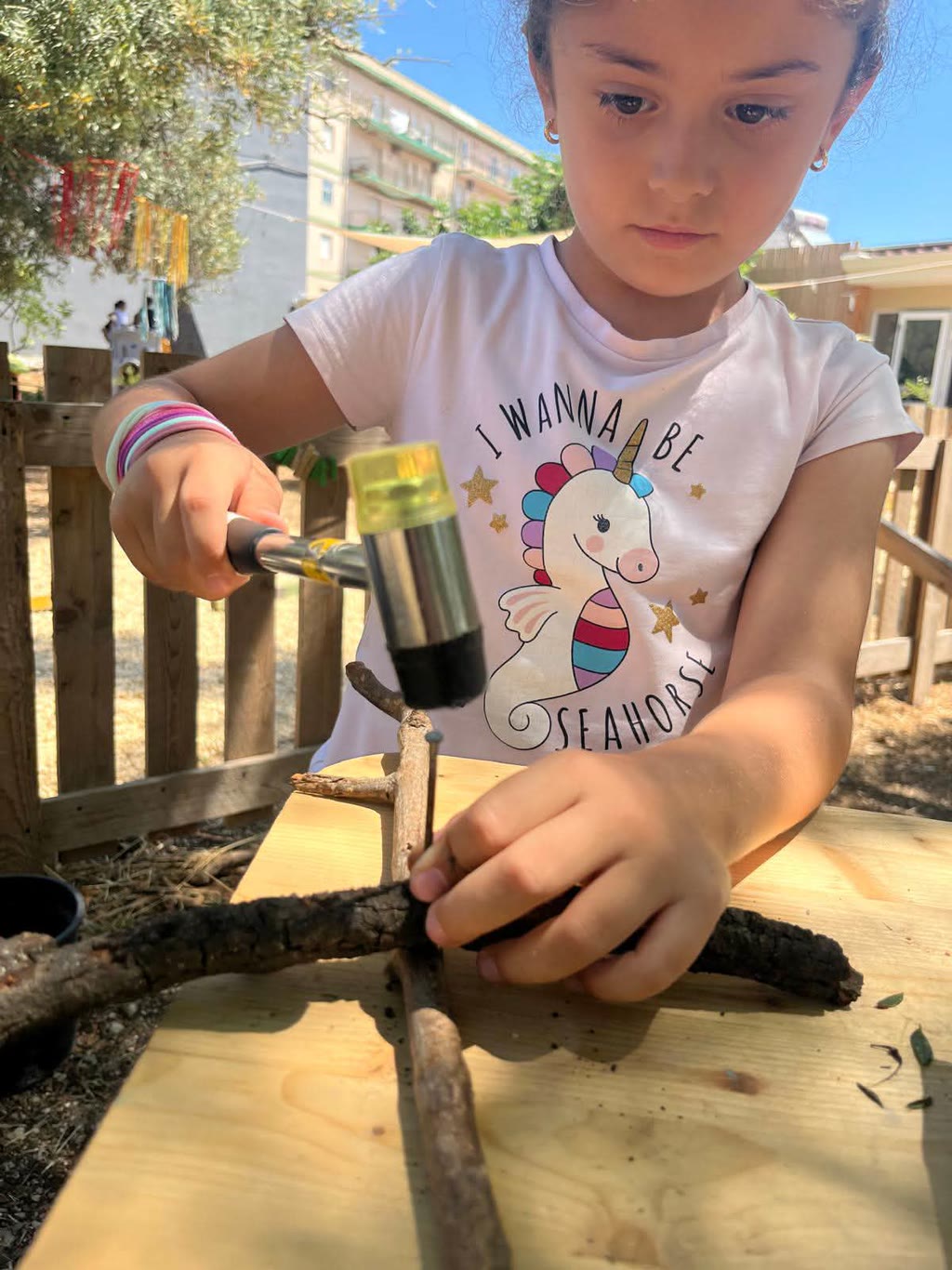 Una bambina lavora con un martello e un rametto su un tavolo di legno