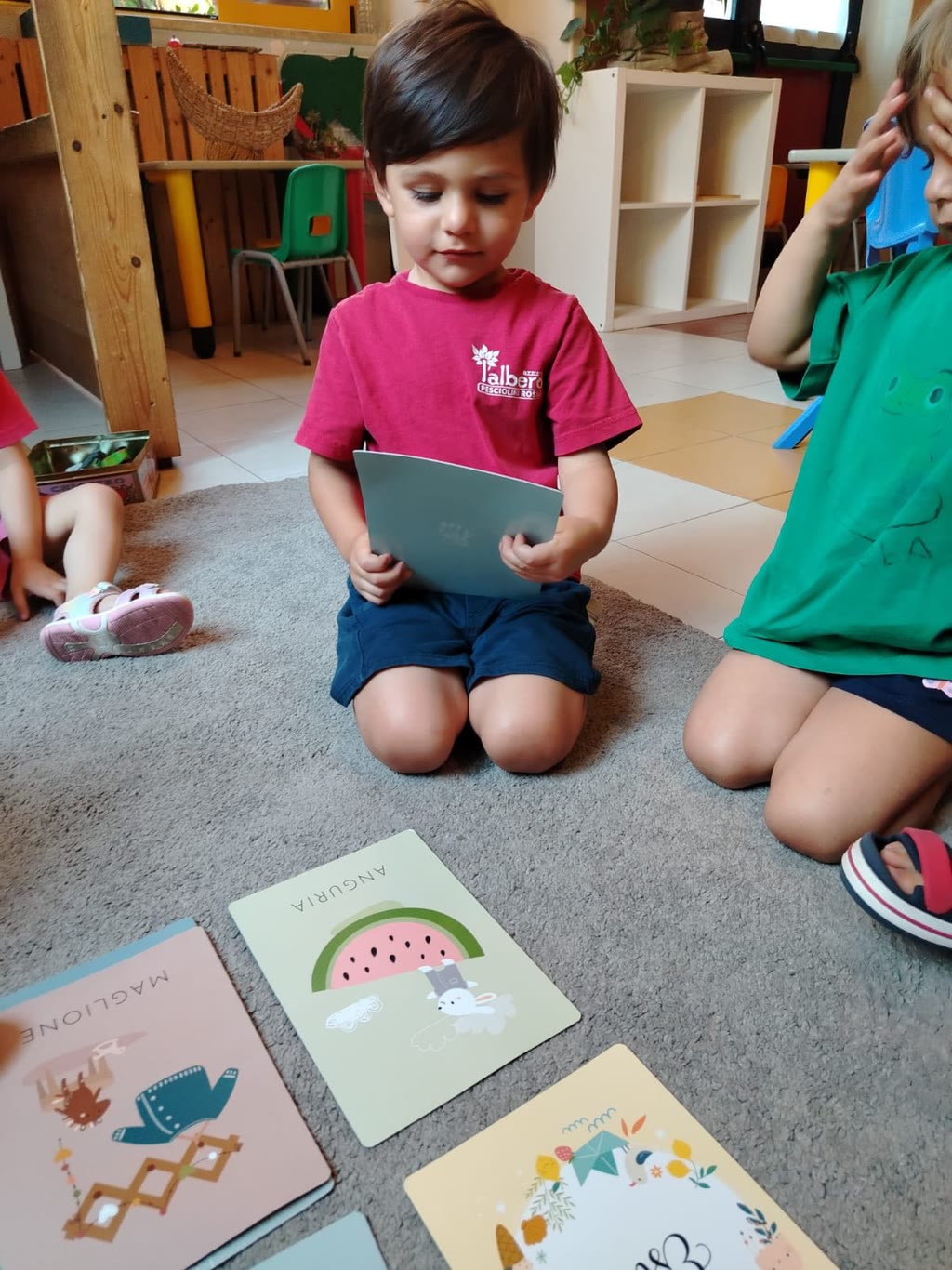 Bambini seduti sul pavimento con carte illustrate, uno legge