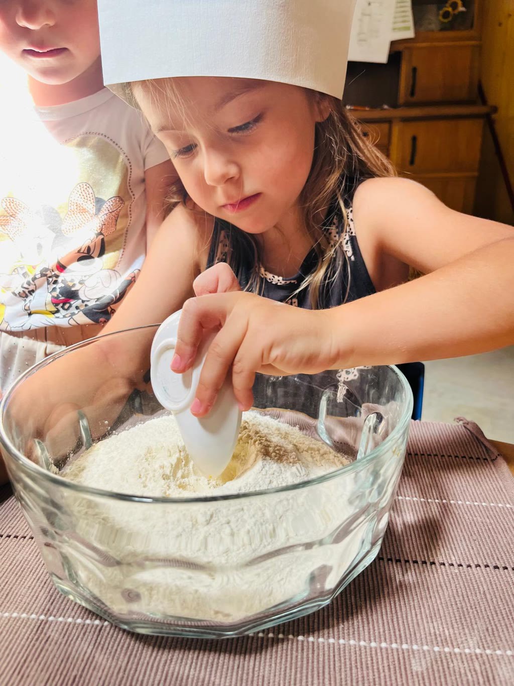 Bambina con cappello da cuoco mescola farina in un grande vassoio di vetro