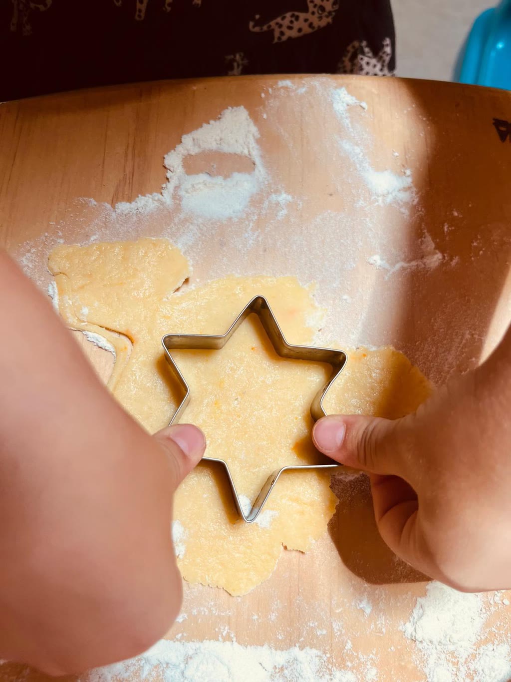Due mani stanno tagliando pasta con un tagliapasta a forma di stella su un tavolo di legno
