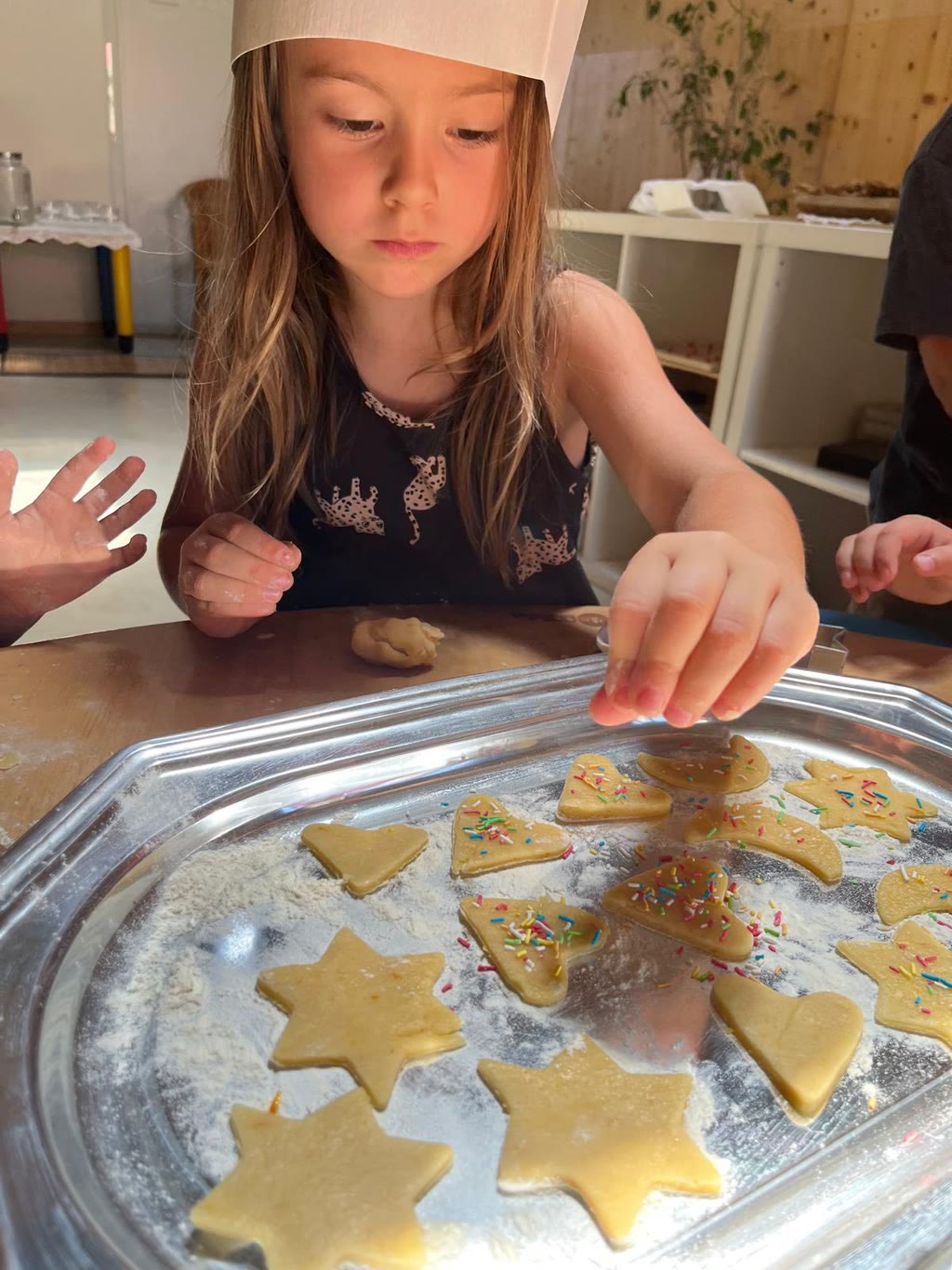 Una bambina prepara biscotti a forma di stelle e cuori su una tegame