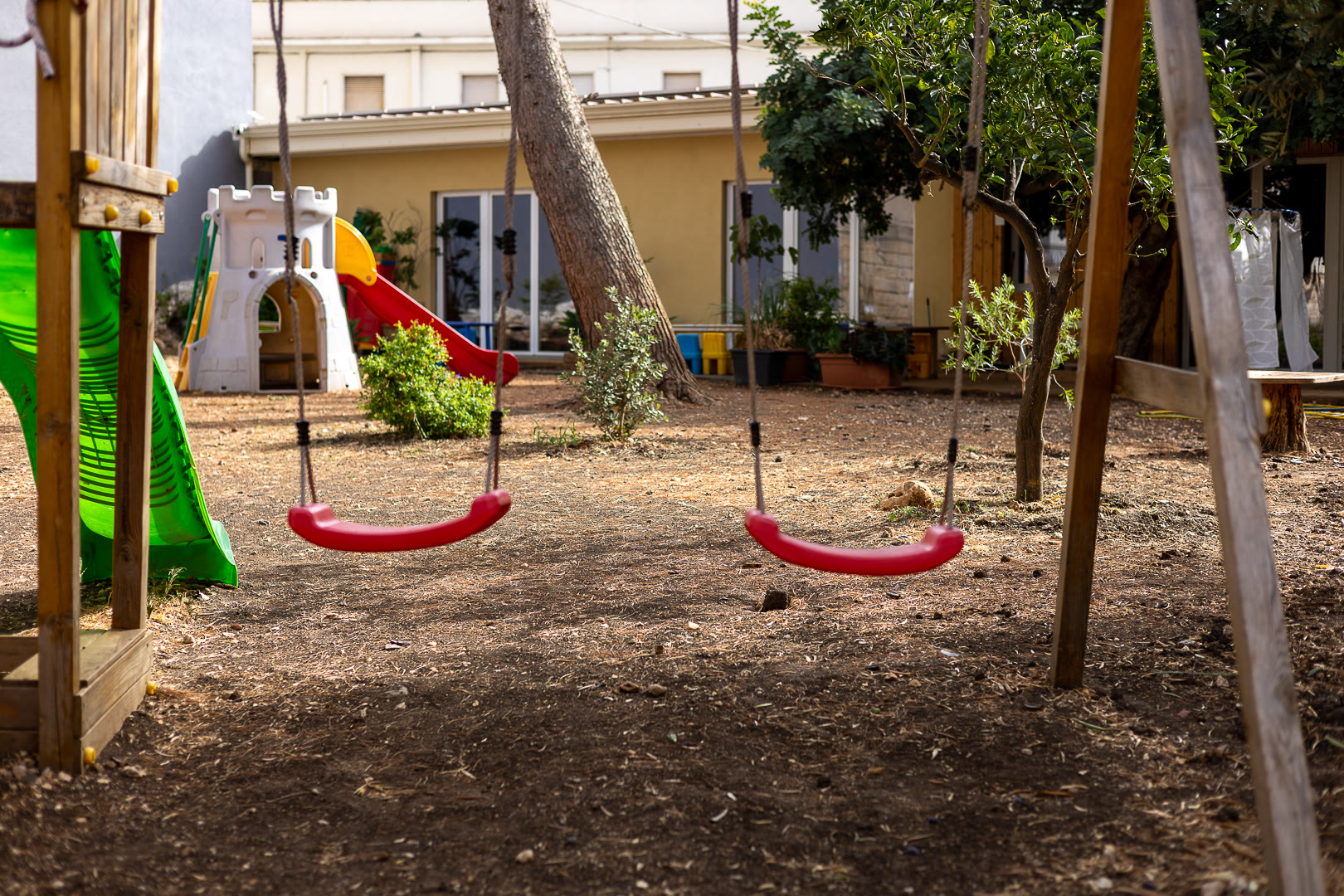 Le altalene e lo scivolo verde sotto gli alberi del giardino.
