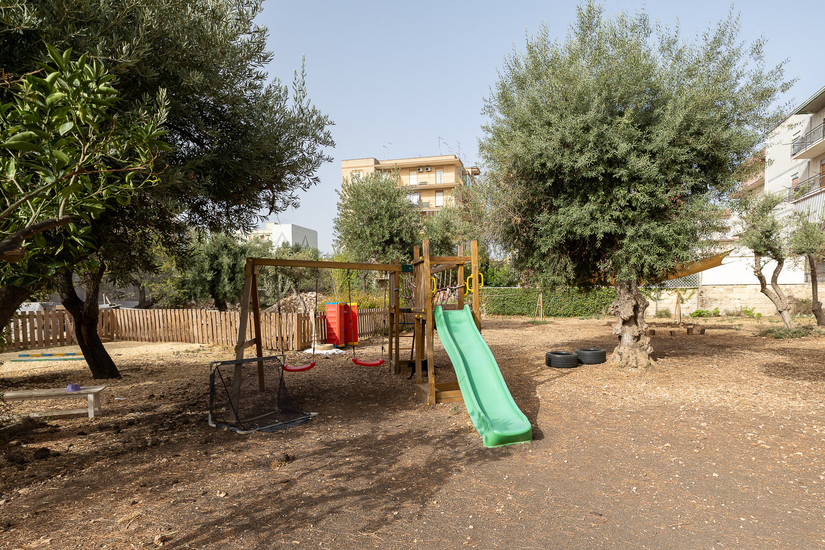 Due altalene rosse appese a una struttura di legno, fra gli alberi del cortile.