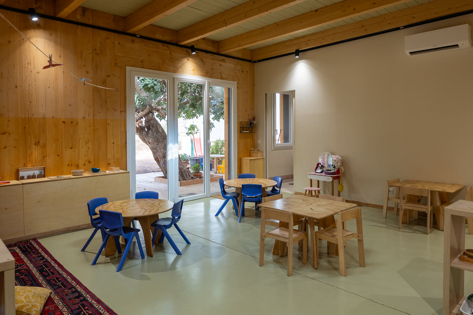 Aula in legno con la grande vetrata sul giardino, i tavoli e le sedie blu.