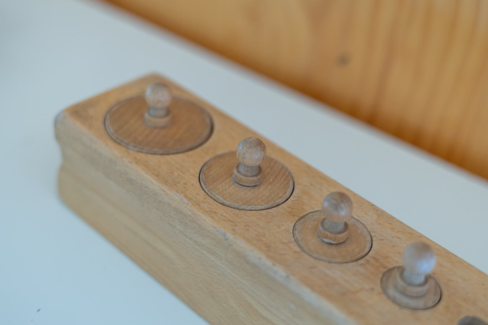 Blocco di legno con i cilindri di diametro decrescente e i pomelli per sfilarli.