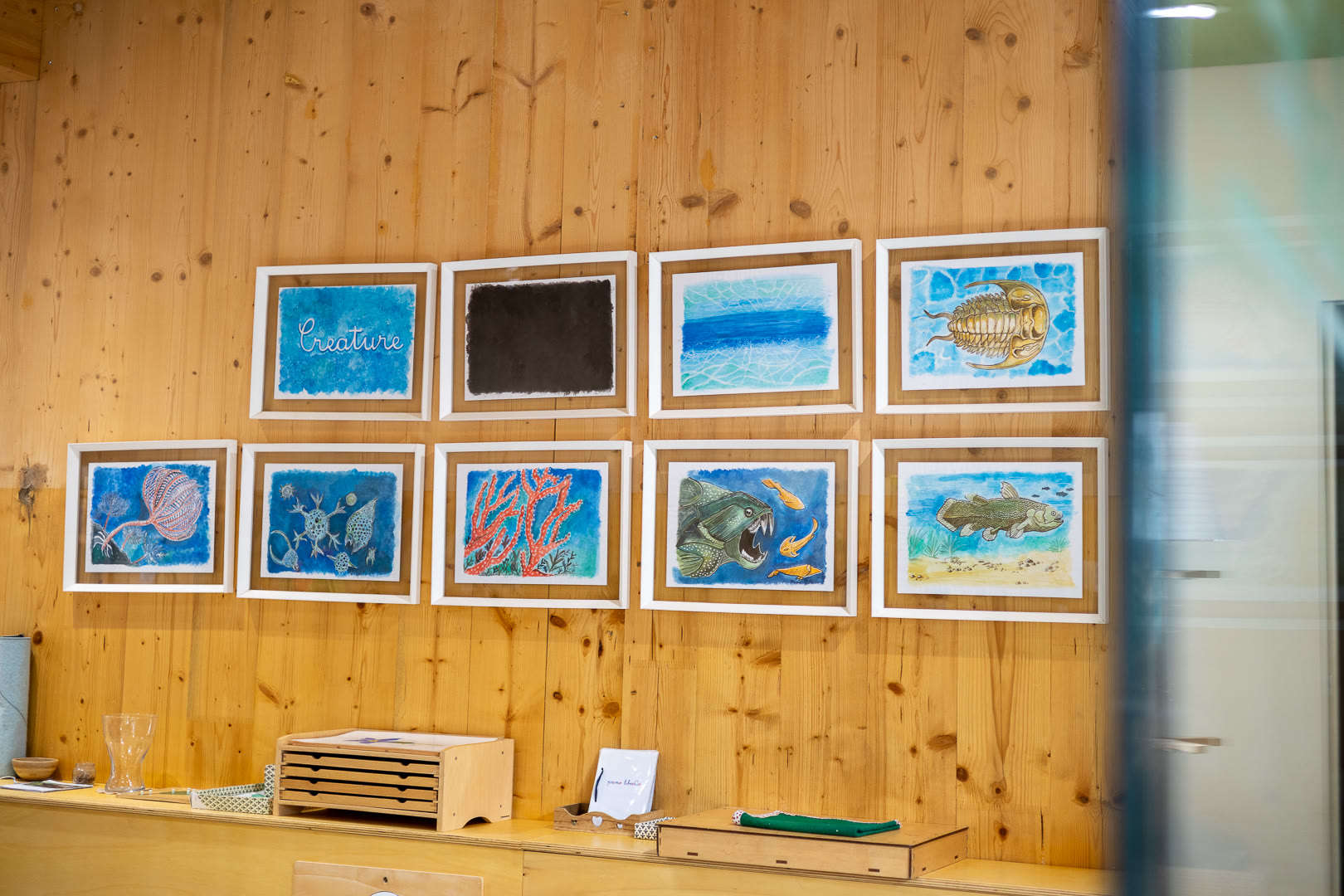 Otto disegni incorniciati appesi in due file sulla parete di legno.