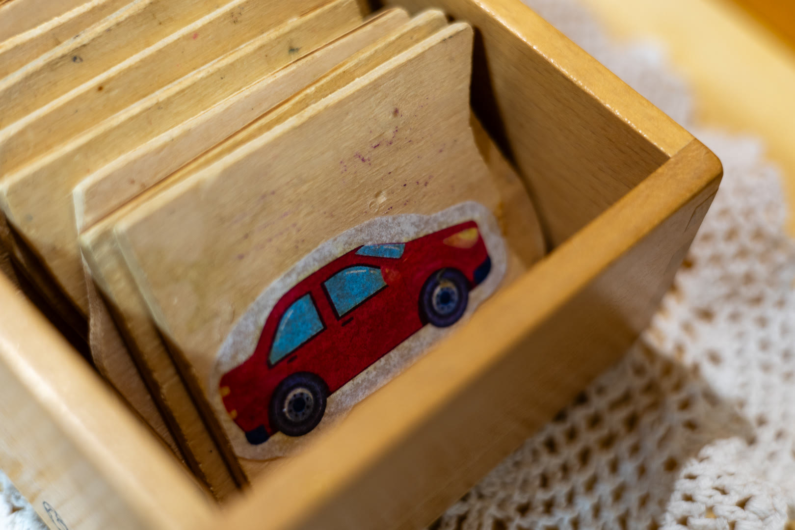 Cassetta di legno con tessere illustrate, in evidenza quella con un'automobile rossa.