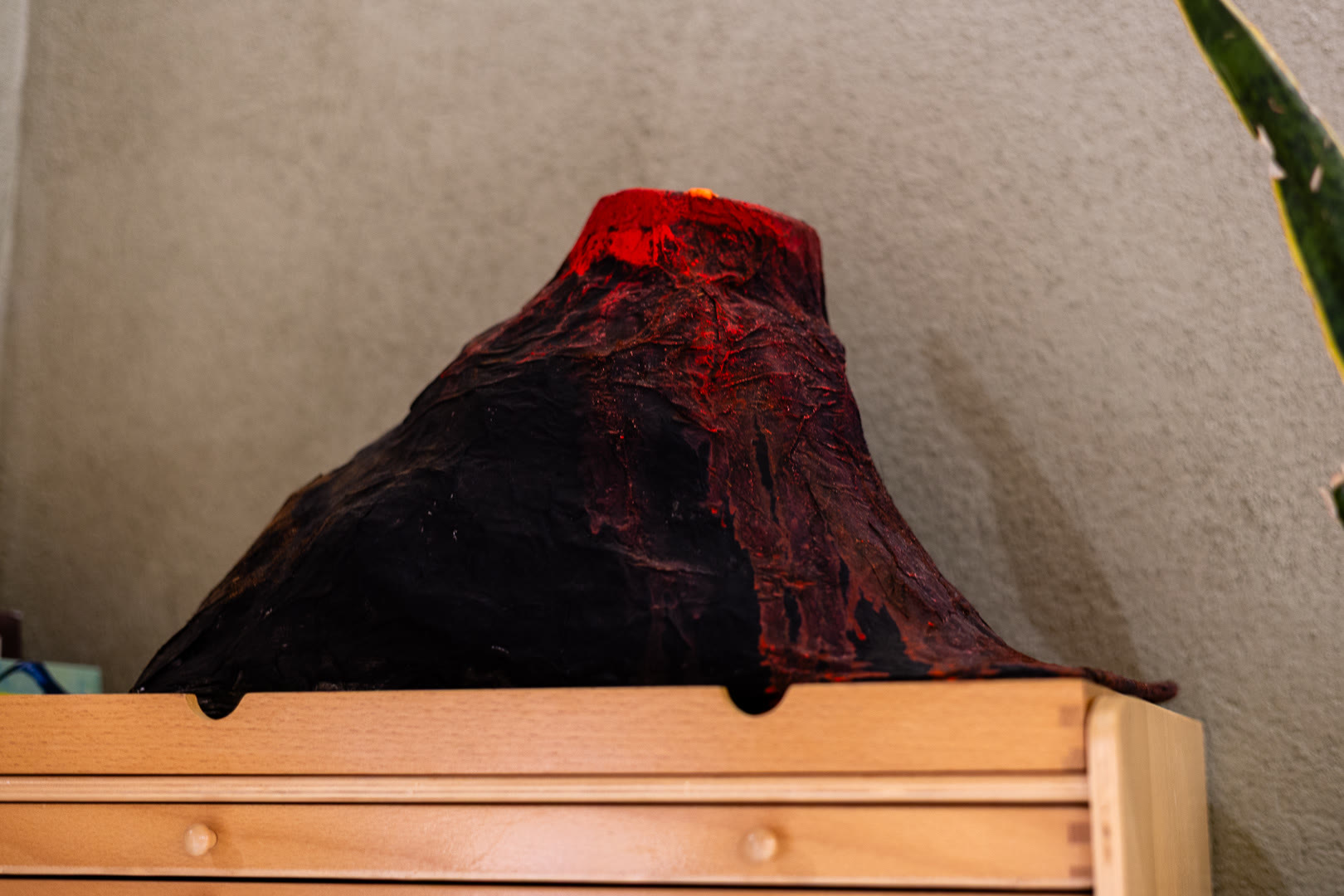 Modello di vulcano con la lava rossa, appoggiato su una mensola di legno.