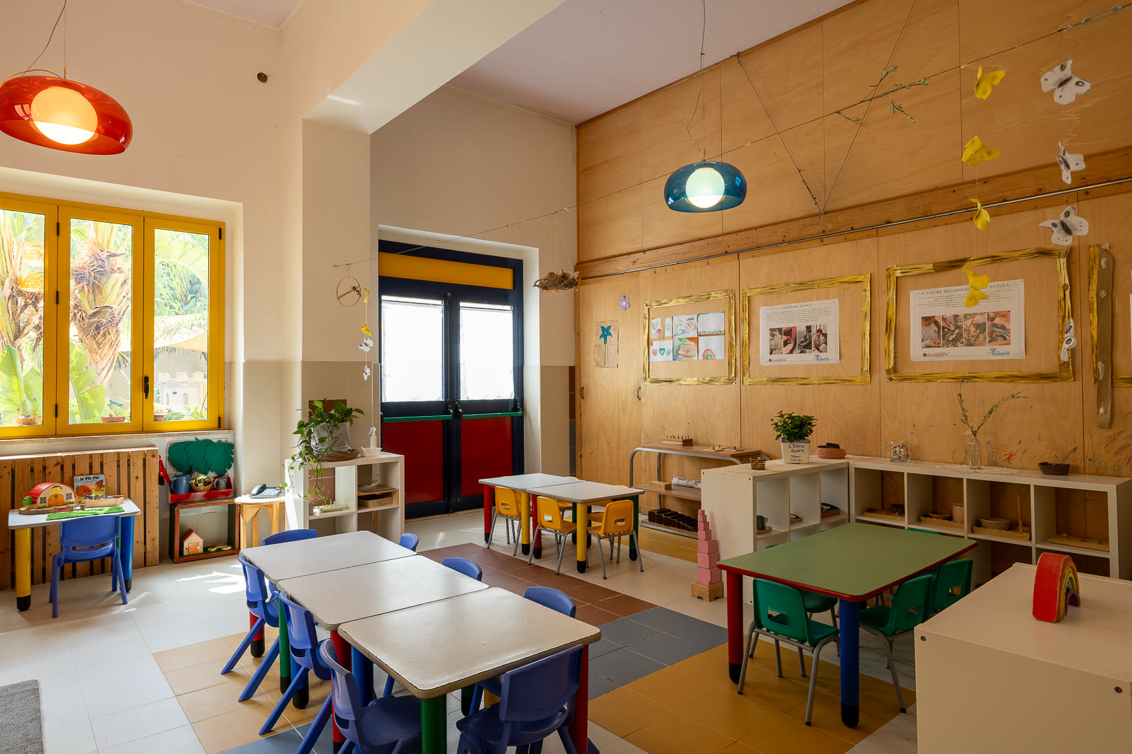 Aula con quadri incorniciati alla parete, tavoli bassi e lampade appese.