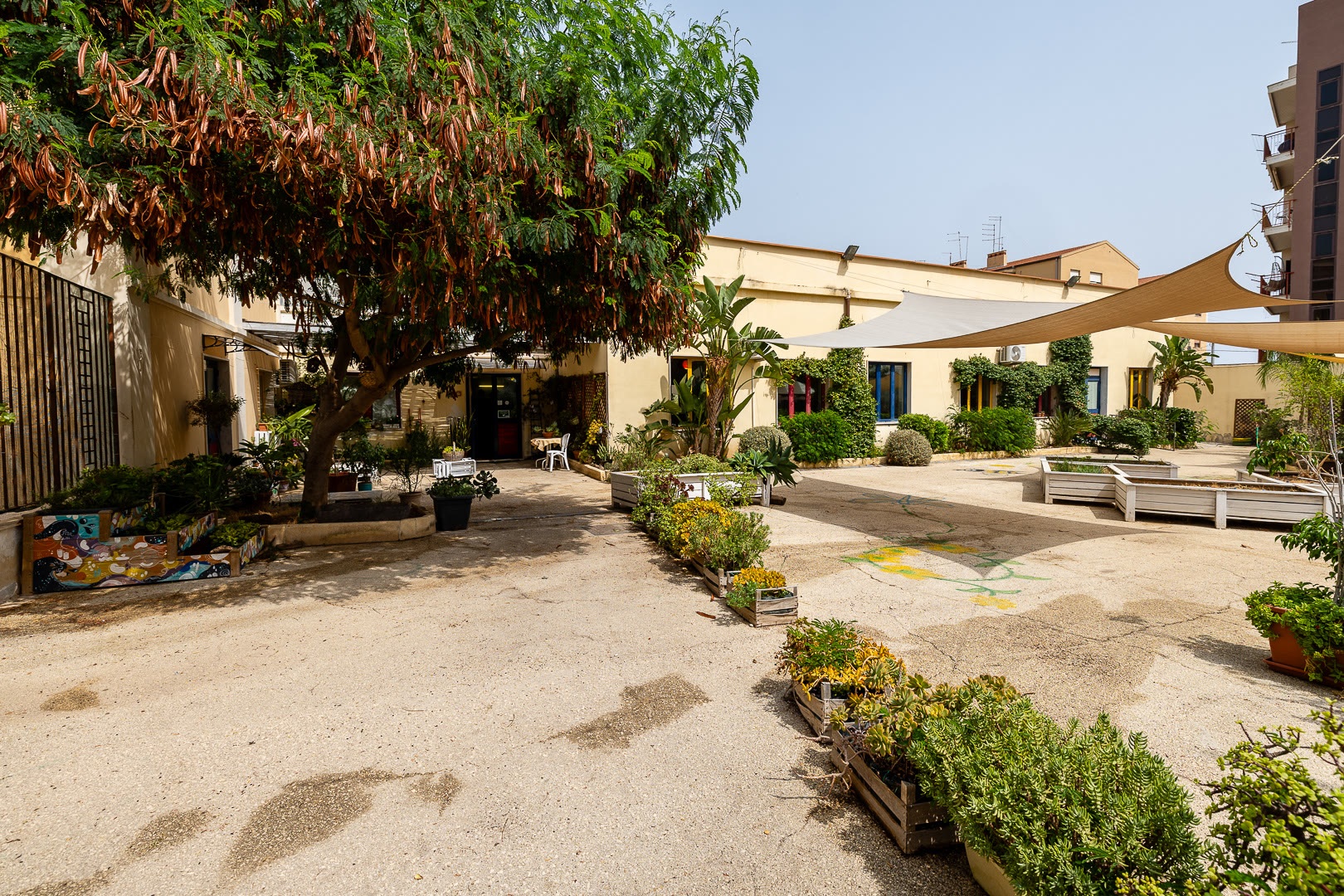 Il cortile interno con le vele ombreggianti, le fioriere in legno e le piante.