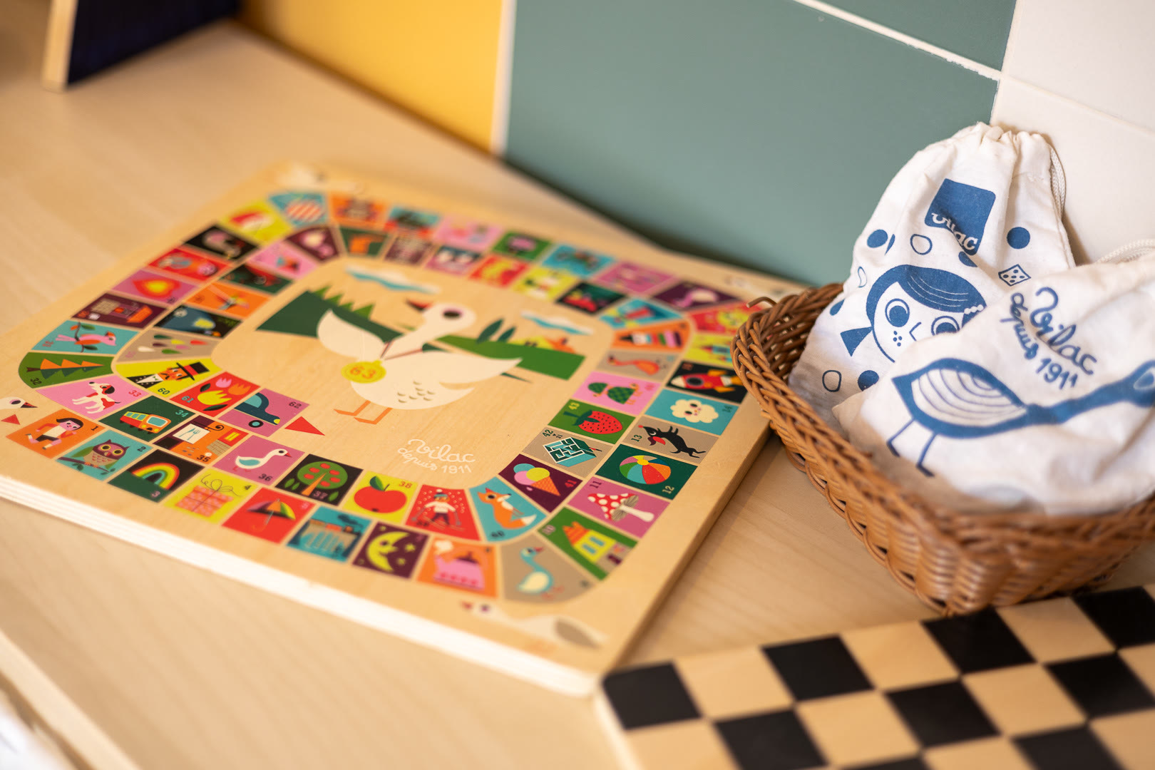 Tabellone del gioco dell'oca in legno, con le caselle illustrate, accanto a un cesto con il sacchetto dei pezzi.