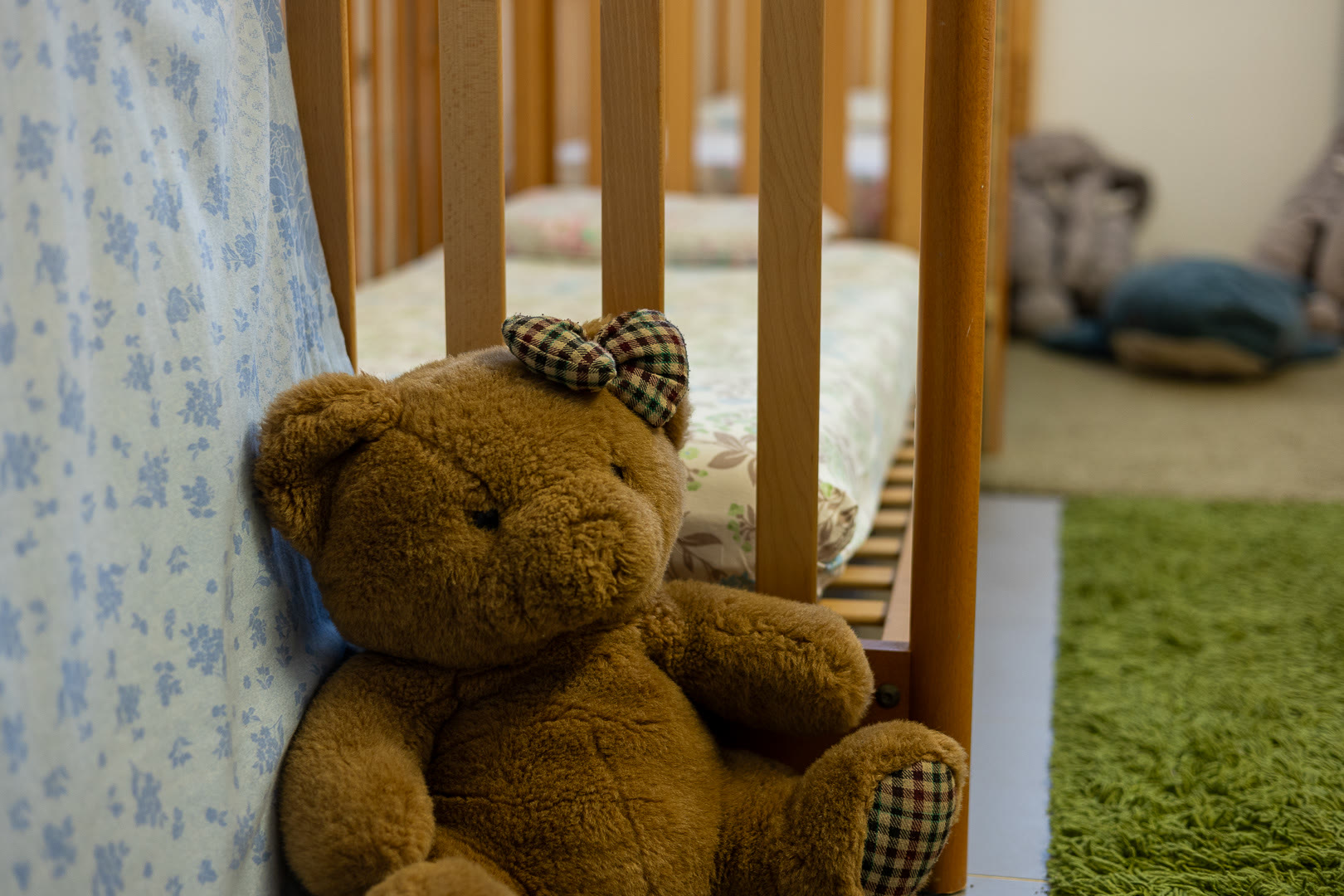 Orsetto di peluche con il fiocco a quadretti, appoggiato alla sponda di un lettino.