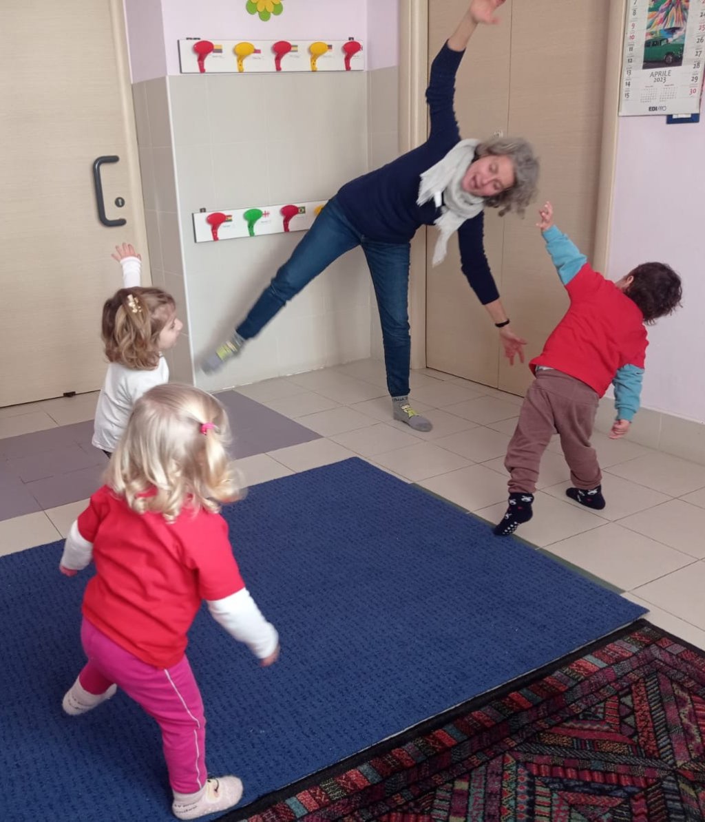Un'insegnante si muove a braccia aperte e i bambini la seguono, imitando il gesto.